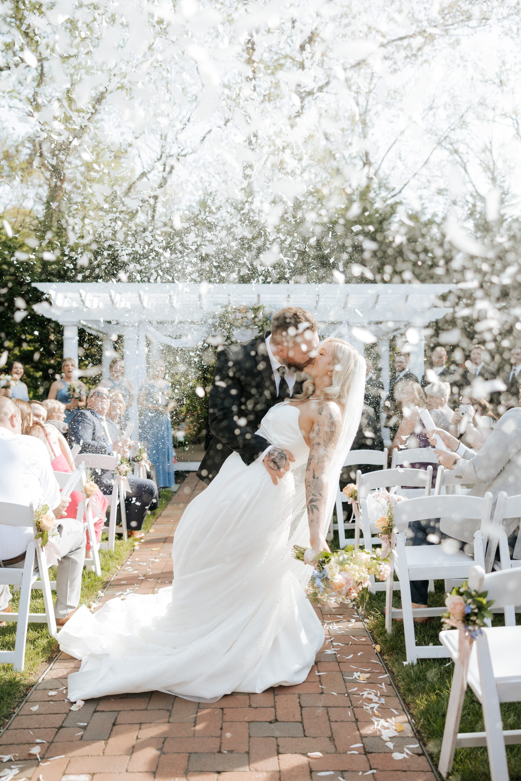 Bride and groom kiss at the end of the aisle with a pop of confetti